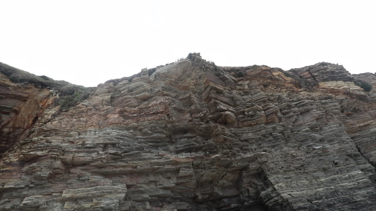 A rugged cliff face with layers of weathered rock formations shot from below on a cloudy day