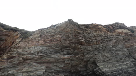 a rugged cliff face with layers of weathered rock formations shot from below on a cloudy day