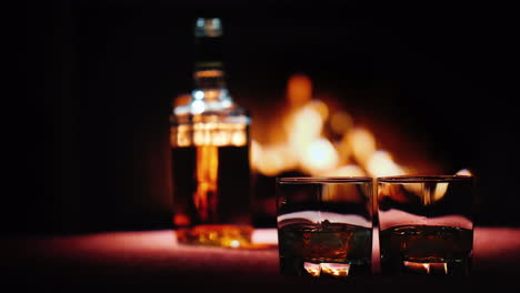 A-Bottle-Of-Strong-Alcohol-Stands-On-The-Table-By-The-Fireplace-In-The-Foreground-Are-Two-Glasses-Of