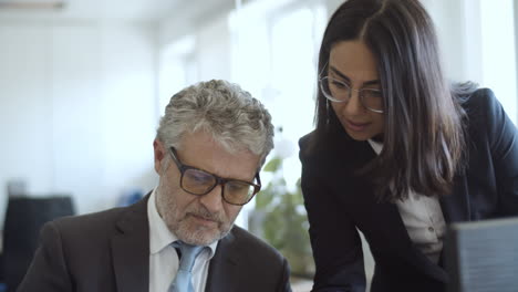 Focused-female-assistant-explaining-paper-details-to-her-boss