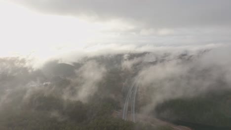imágenes de drones de la carretera y la urbanización en noruega con algo de niebla flotando en el aire y el sol iluminando las nubes