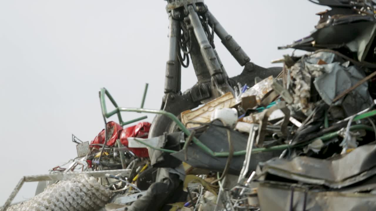 Crane lifting scrap metal at a recycling yard with a cloudy sky in the background