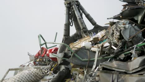 crane lifting scrap metal at a recycling yard with a cloudy sky in the background
