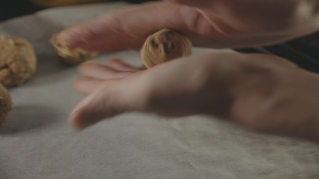 manos rodando masa para galletas y colocándolas en una bandeja con una bandeja para hornear - cerrar