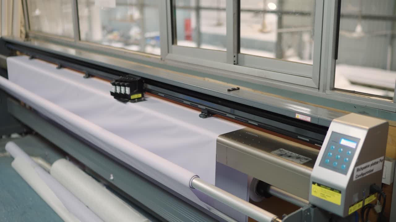 Left moving camera clip showing a large inkjet plotter machine working inside a tent manufacturing factory in Sialkot, Pakistan