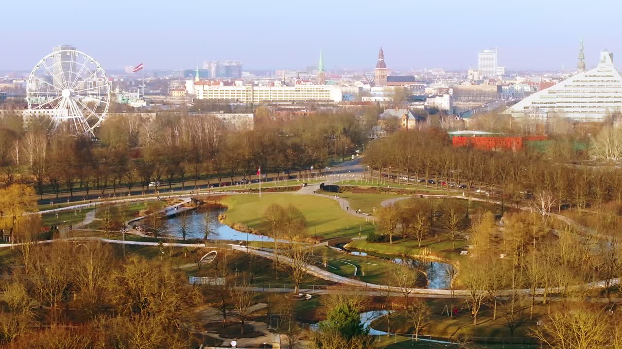 Drone swiftly pans left revealing Riga's skyline and lush Victory Park below