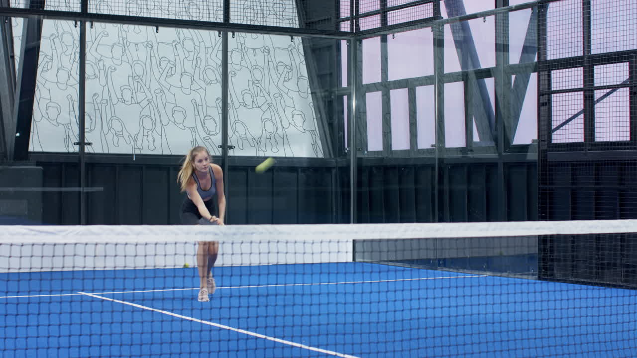 Woman playing padel tennis on blue indoor court, focused and ready for action