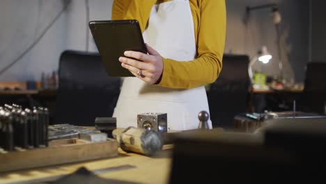 Mittelteil-Einer-Kaukasischen-Juwelierin-In-Der-Werkstatt,-Die-Eine-Schürze-Trägt-Und-Ein-Tablet-Benutzt