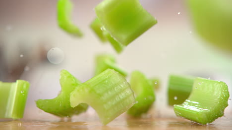 chopped celery falling onto the wooden table, bouncing and splashing water droplets around the kitchen in macro and slow motion