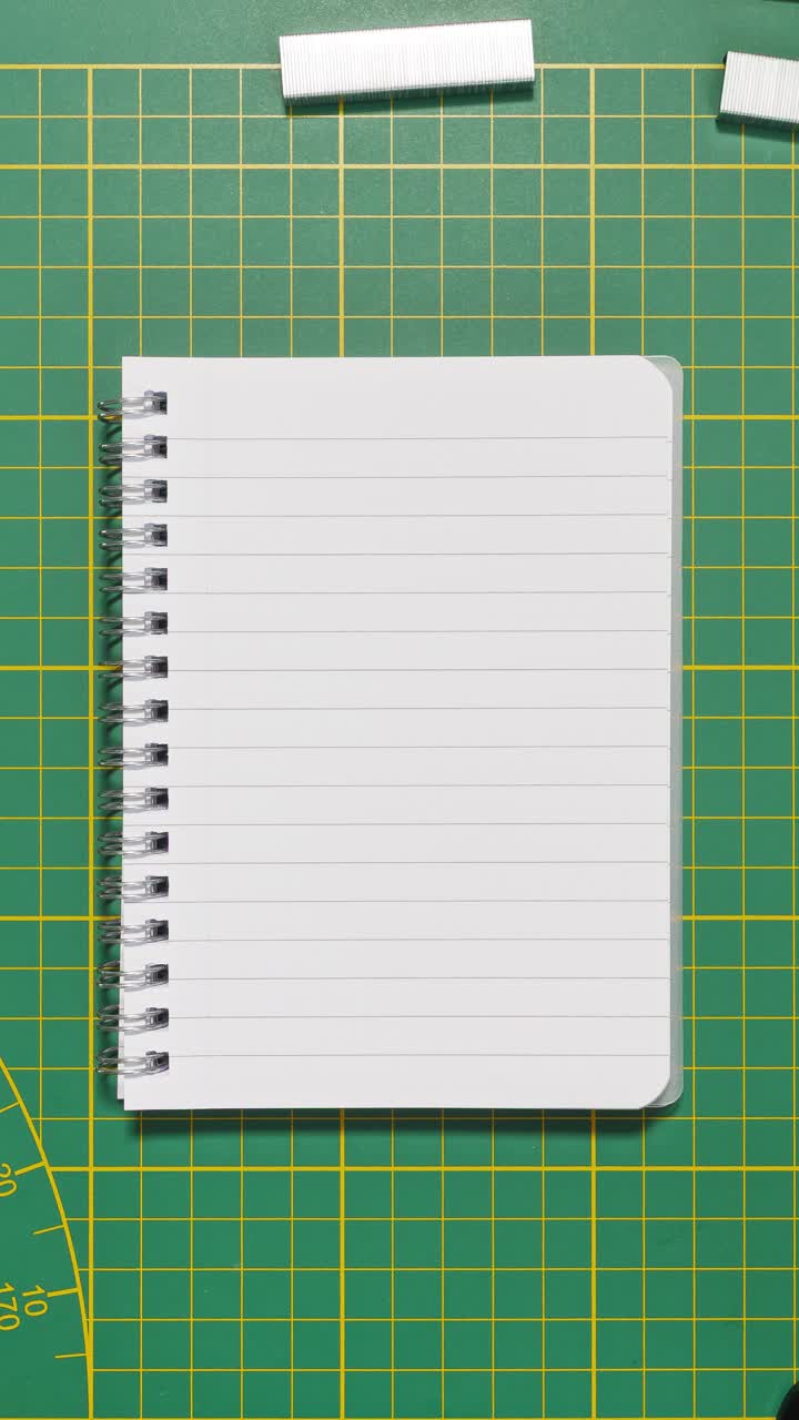 Portrait stop-motion loop of stationery framing a lined spiral notebook on a green cutting mat with central copy space