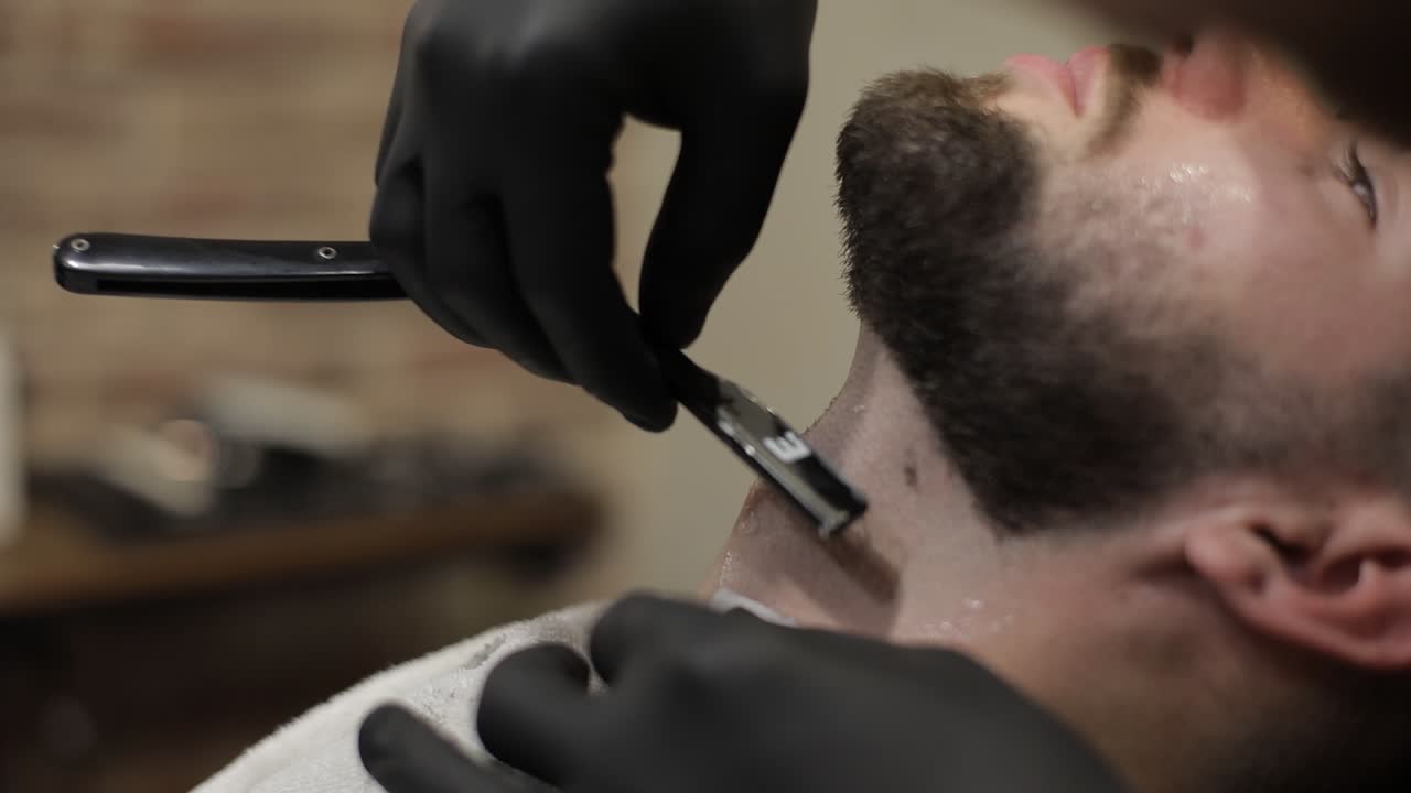 Cliente com barba preta durante o barbear na barbearia. Homem, masculino.