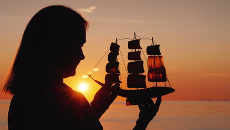 Perfil-De-Una-Mujer-Con-Un-Velero-De-Juguete-Contra-La-Atardecer