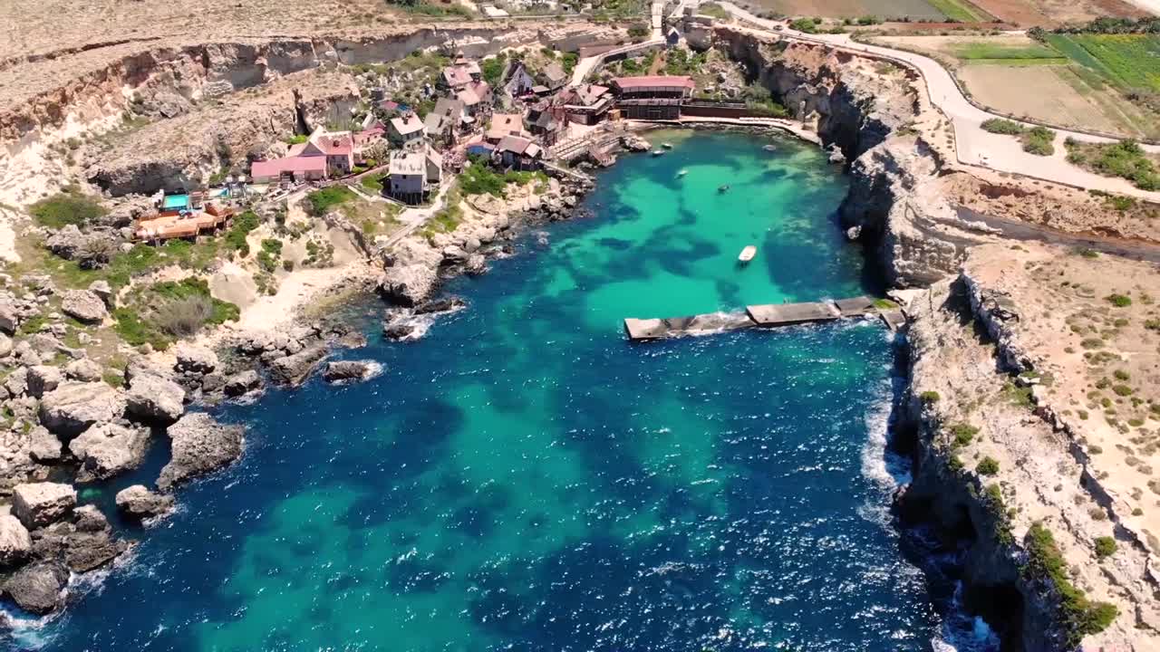 Beautiful small fishing village aerial birds eye shot fly backward bay reveal. Popeye village filming location, Malta.