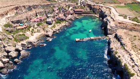 beautiful small fishing village aerial birds eye shot fly backward bay reveal. popeye village filming location, malta.