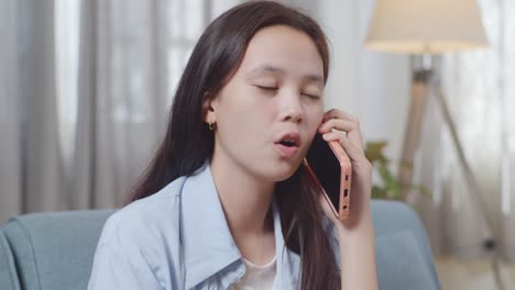 close up of asian teen girl talking on smartphone while sitting on sofa in the living room at home