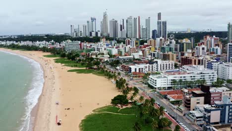 Tilting-up-dolly-out-aerial-drone-shot-of-the-cityscape-of-the-colorful-tropical-beach-capital-city-of-Joao-Pessoa-in-Paraiba,-Brazil-from-the-Tambaú-neighborhood-on-an-overcast-morning