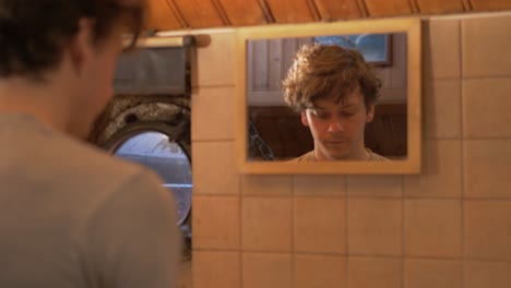 Young-man-walks-to-mirror-washing-hands-in-sink