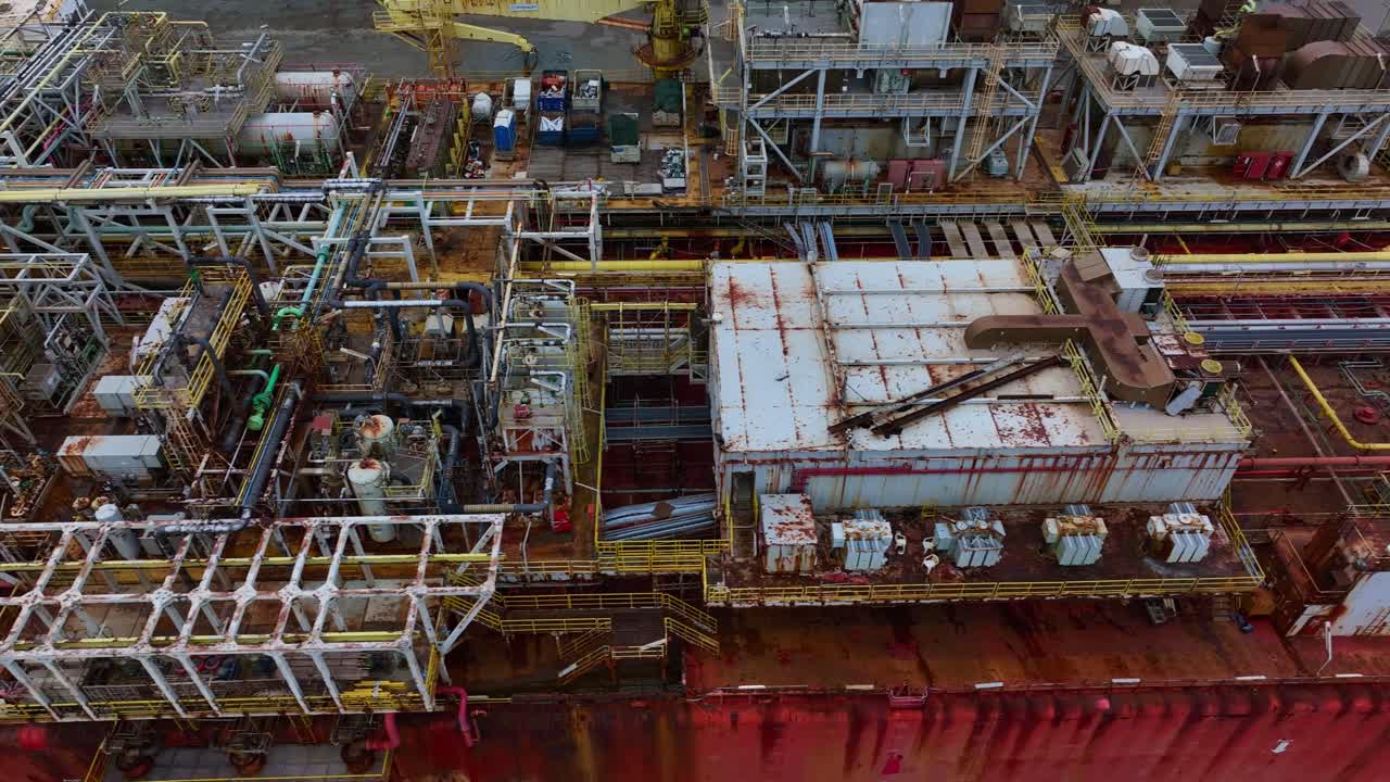 Aerial drone footage of a red tanker with a rust-covered deck, showing old industrial equipment and corroded pipes.
