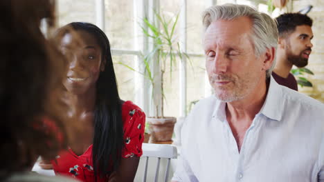 Senior-white-man-and-young-black-woman-sitting-at-a-table-in-a-restaurant-during-the-day-talking-with-friends,-close-up