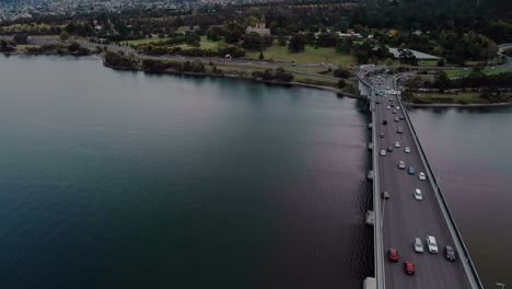 Aerial-tilt-shot-of-a-busy-bridge-with-mountains-and-cityscape-at-background