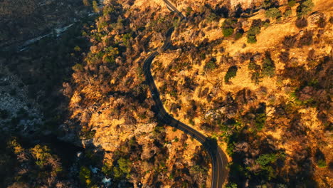 Car riding by the wavy highway in the mountains. Sunlit rocks of California from top perspective.