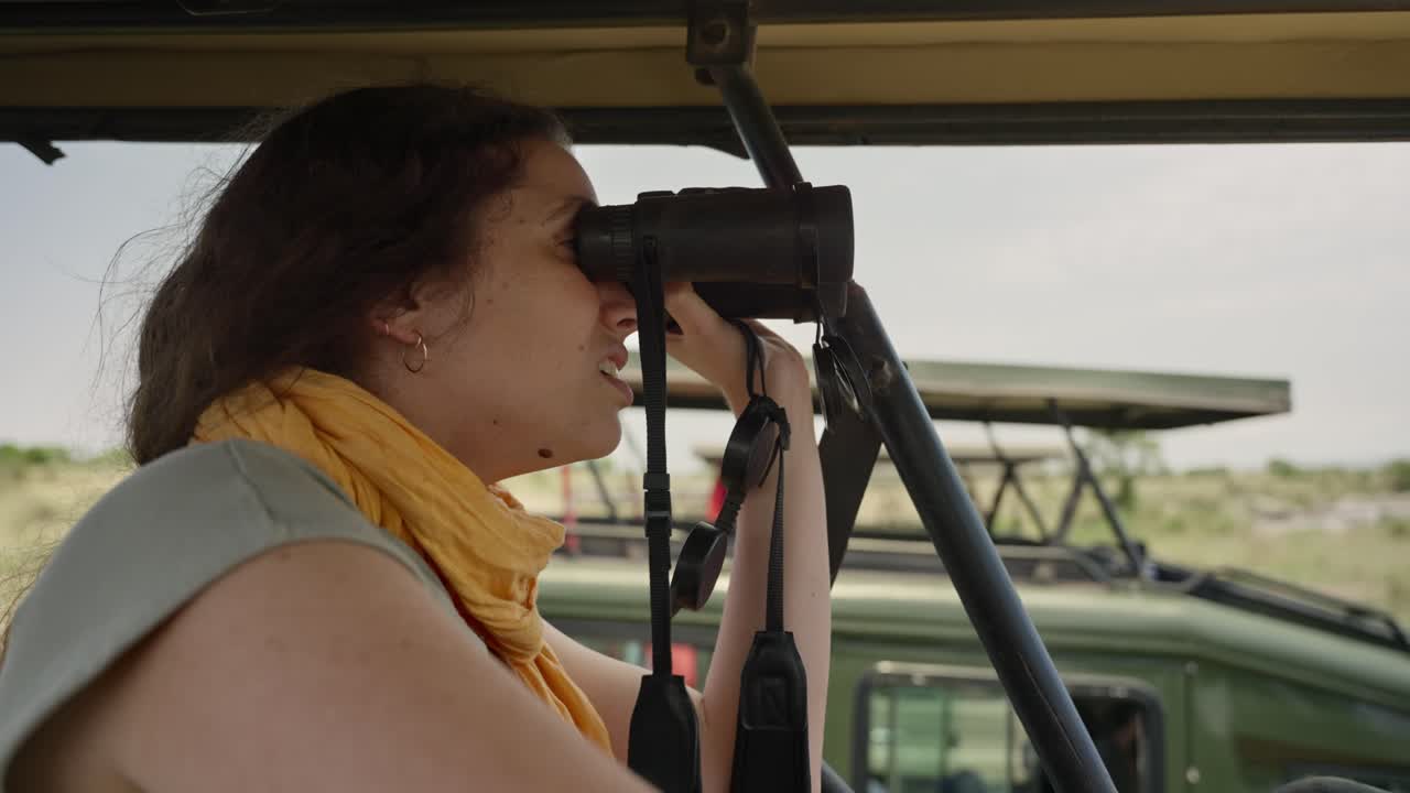 Young tourist in Safari vehicle looking at nature and wild animals in Africa. Standing inside special 4x4 off road vehicle female explorer or researcher watching wildlife in Serengeti National Park