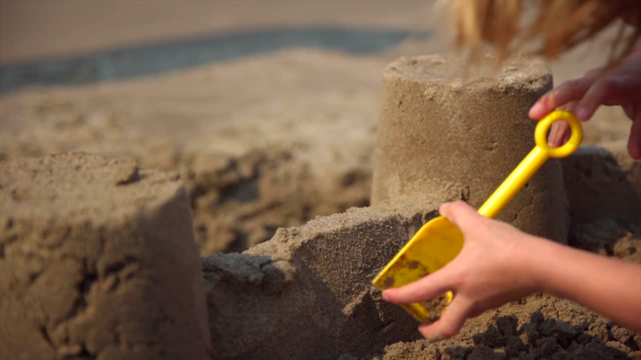 Child making sandcastle on the beach with yellow shovel