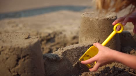 niño haciendo un castillo de arena en la playa con una pala amarilla