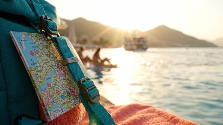 Ein malerischer Abend am Wasser: Ein Rucksack mit einer Karte blickt auf einen wunderschönen Sonnenuntergang und entspannte Strandbesucher an einem ruhigen Küstenort.