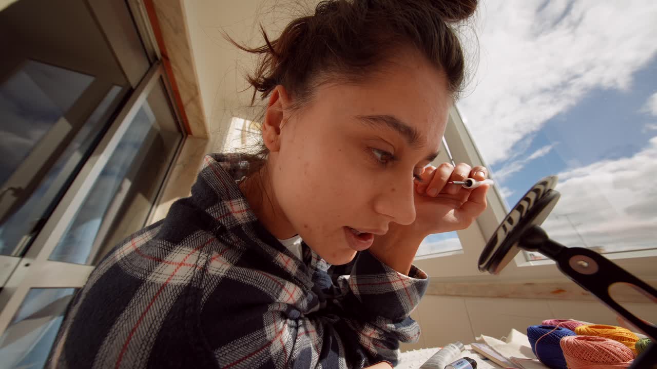 Giovane donna giocosa che applica l'eyeliner vicino alla finestra.