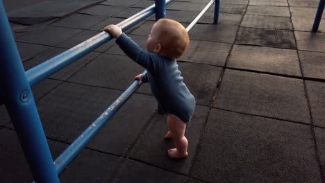 happy toddler boy stands up on his own using blue jungle gym bars