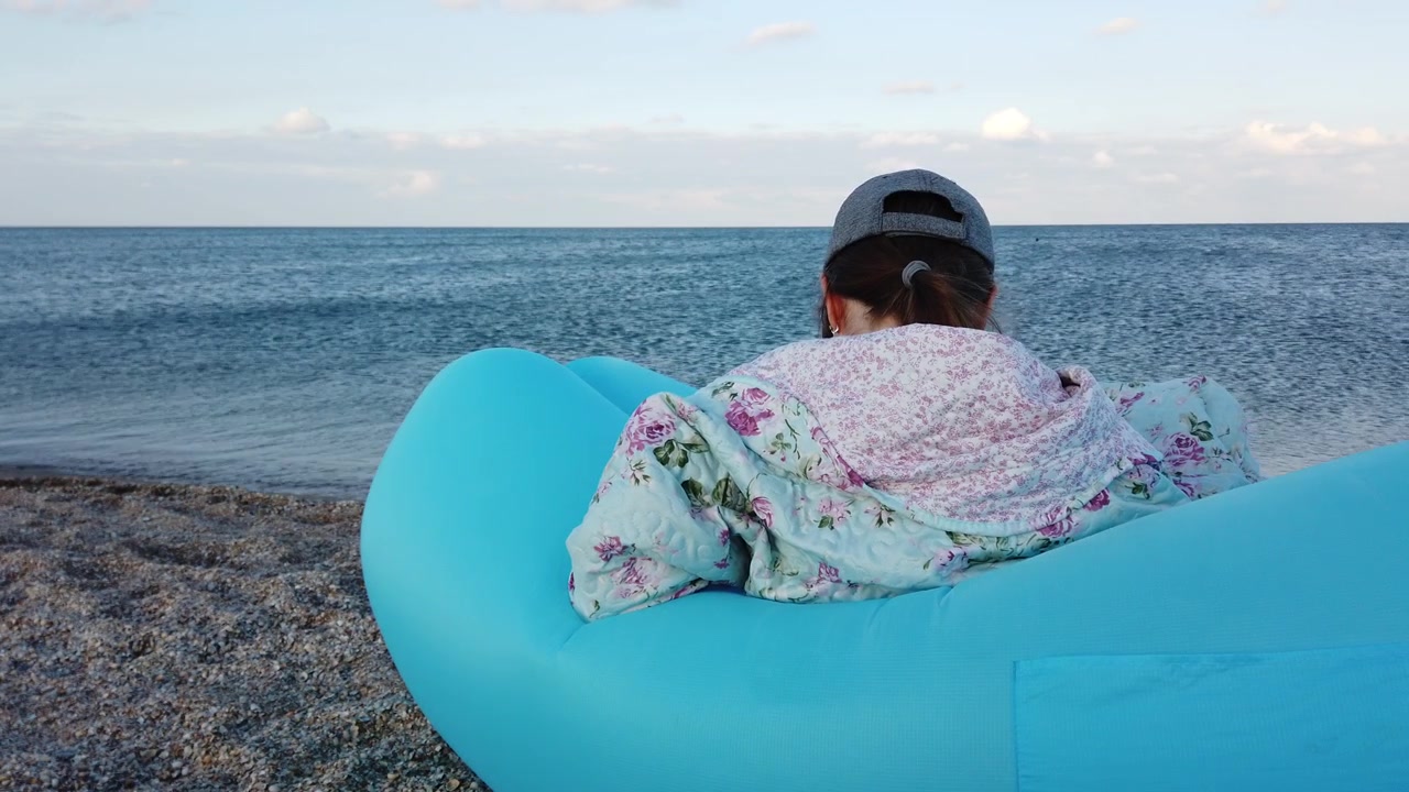 Una ragazza sulla spiaggia si siede su un'amaca gonfiabile.