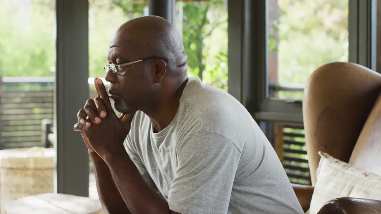Thoughtful african american senior man in living room sitting in armchair contemplating