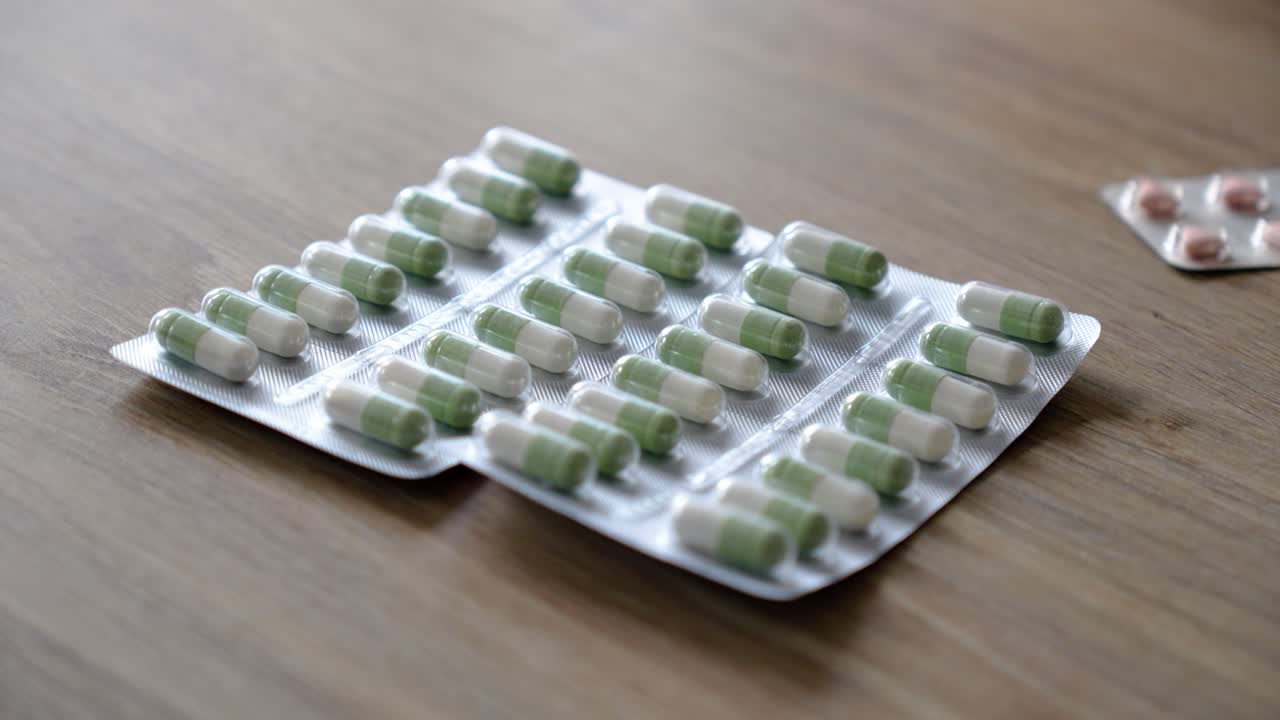 close-up of two aluminium and plastic plates filled with white and green capsules on a wooden table