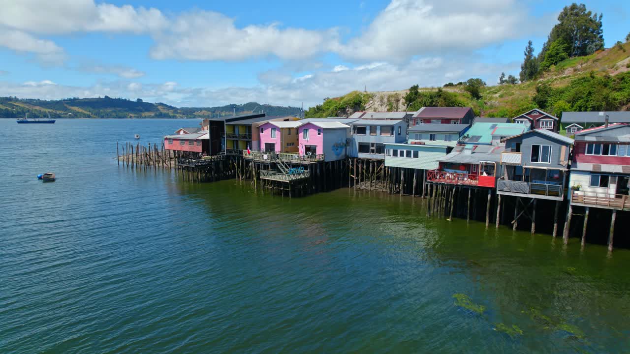 카스트로 (castro), 칠로 (chiloe) 에서 물 위에 있는 다채로운 기둥집들은 부분적으로 구름이 가득한 하늘 아래 독특한 숙박 시설을 제공합니다.