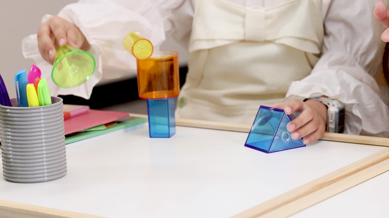 Person manipulates translucent 3D geometric solids on a white tabletop under bright, even lighting