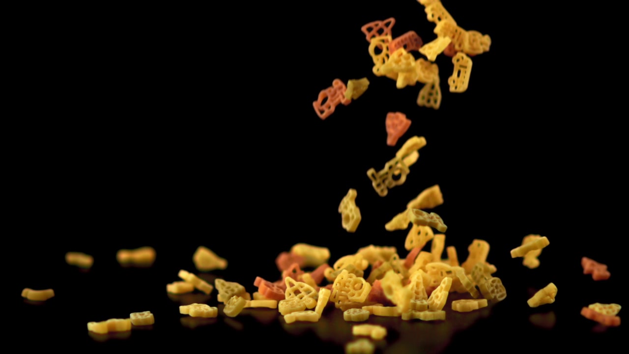 Pasta colorata sagomata che cade su una superficie nera al rallentatore