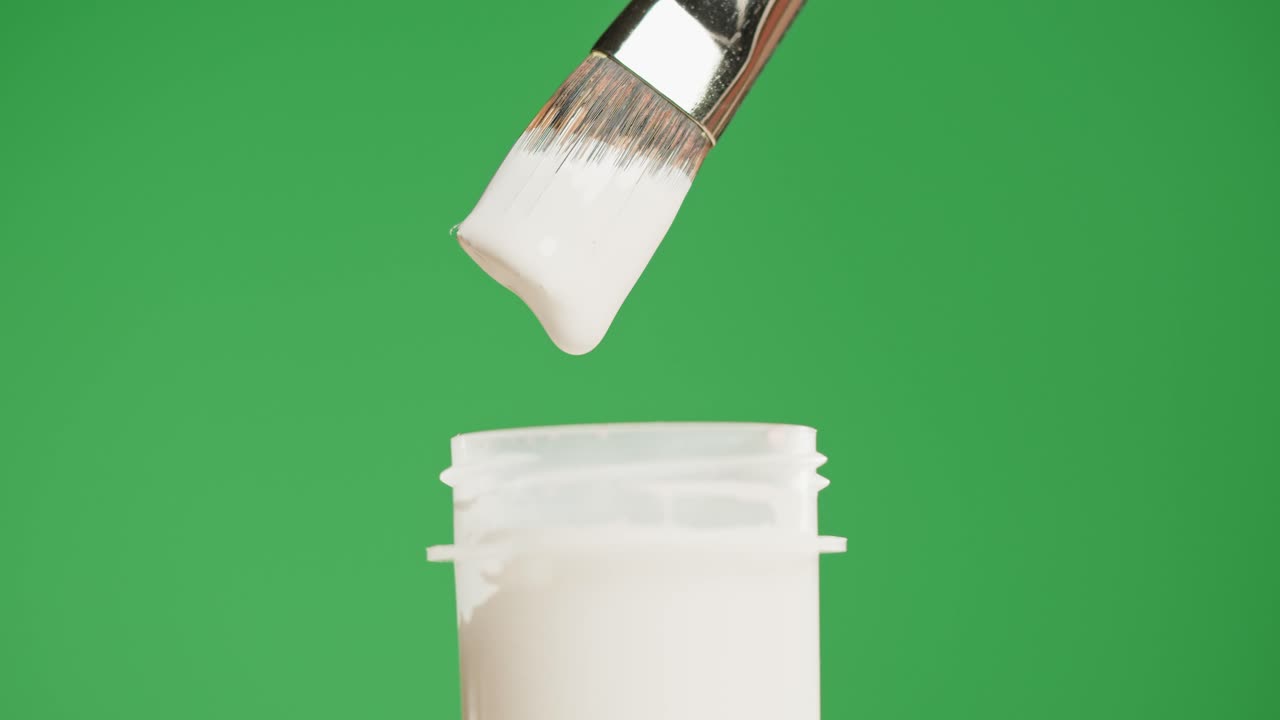 Witte verf die van een penseel in een pot druppelt op een groen scherm.