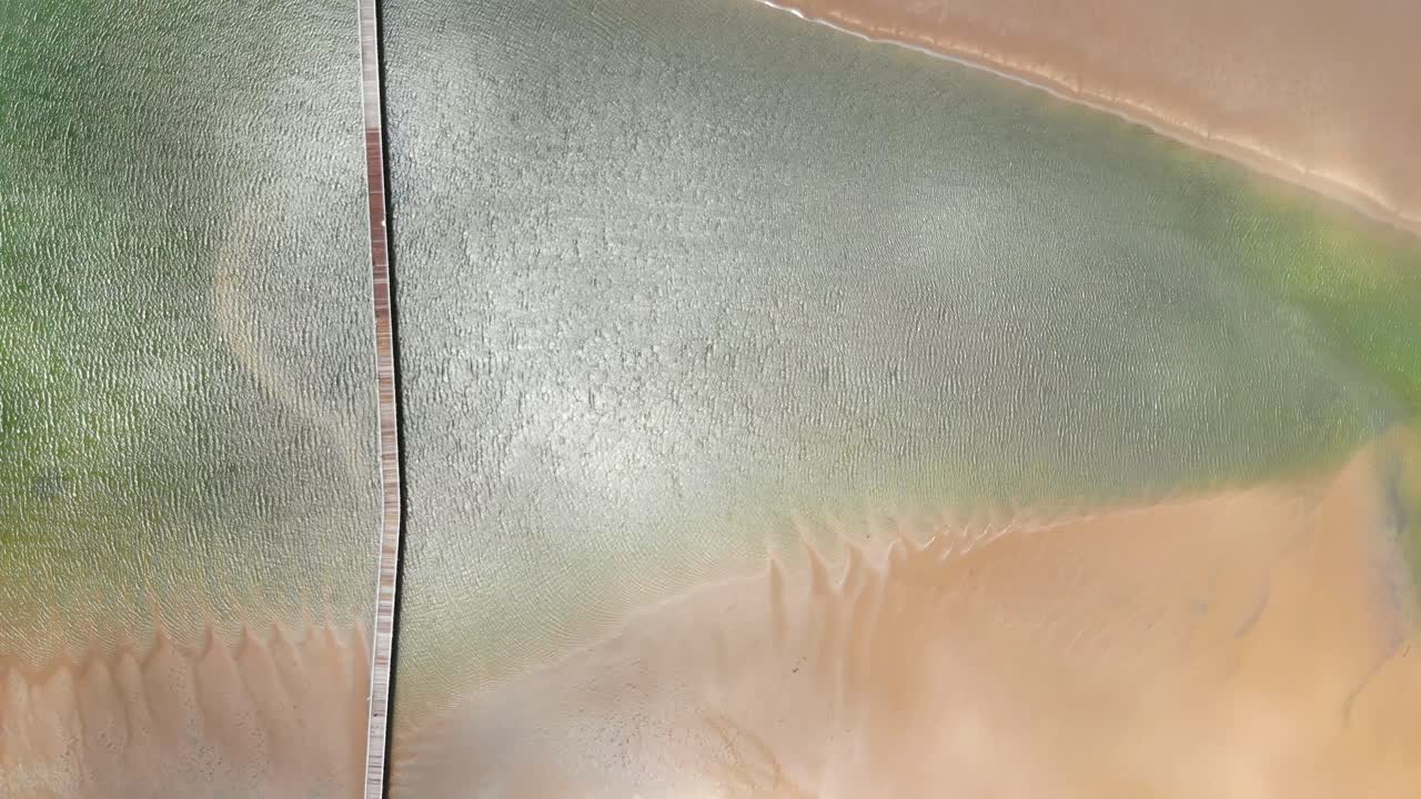 따뜻하고 화창한 날에 결국 바다로 여행하기 위해 모래와 수역을 가로질러 뻗어 있는 길고 오래된 목재 부두의 하향식 비행