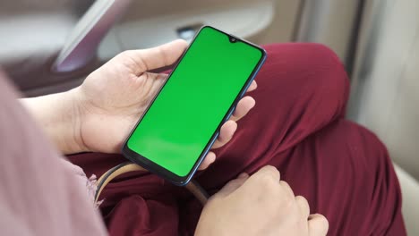 woman holding smartphone with green screen in a car