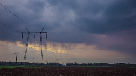 Rain-clouds-flow-above-high-voltage-power-lines-in-agriculture-landscape,-time-lapse