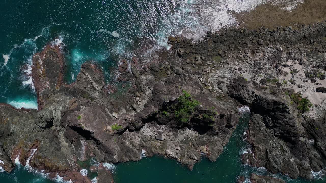 A top dolly-out drone shot gracefully pulls back from the small rocky mountains along the shore, revealing more of the rugged coastline and the endless ocean beyond.