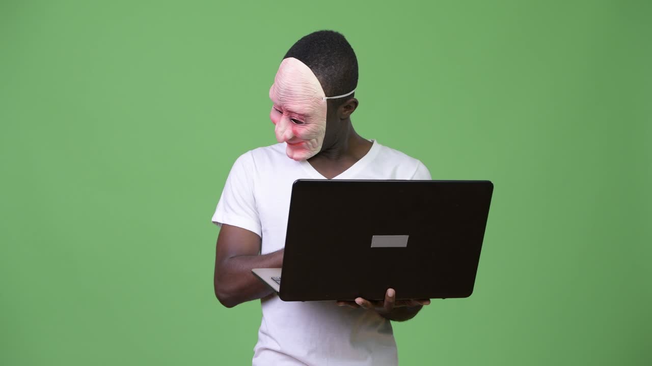 Junger afrikanischer Mann trägt Maske und benutzt Laptop.
