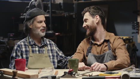 portrait shot of cheerful father and son in goggles with thumbs up and looking at camera in workroom