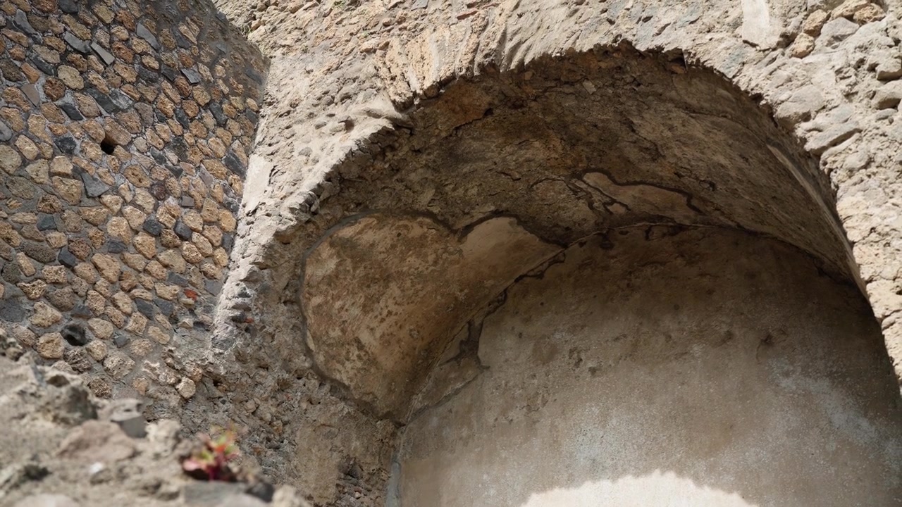 Vista dal basso di una nicchia a volta crepata a Pompei, che evidenzia l'intonaco romano antico, la muratura curva e i dettagli archeologici usurati alla calda luce del giorno