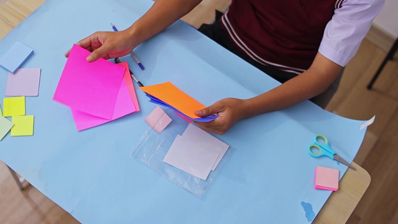 Inquadratura dall'alto di uno studente che organizza fogli di carta quadrati colorati per lavoretti fai da te o per studio