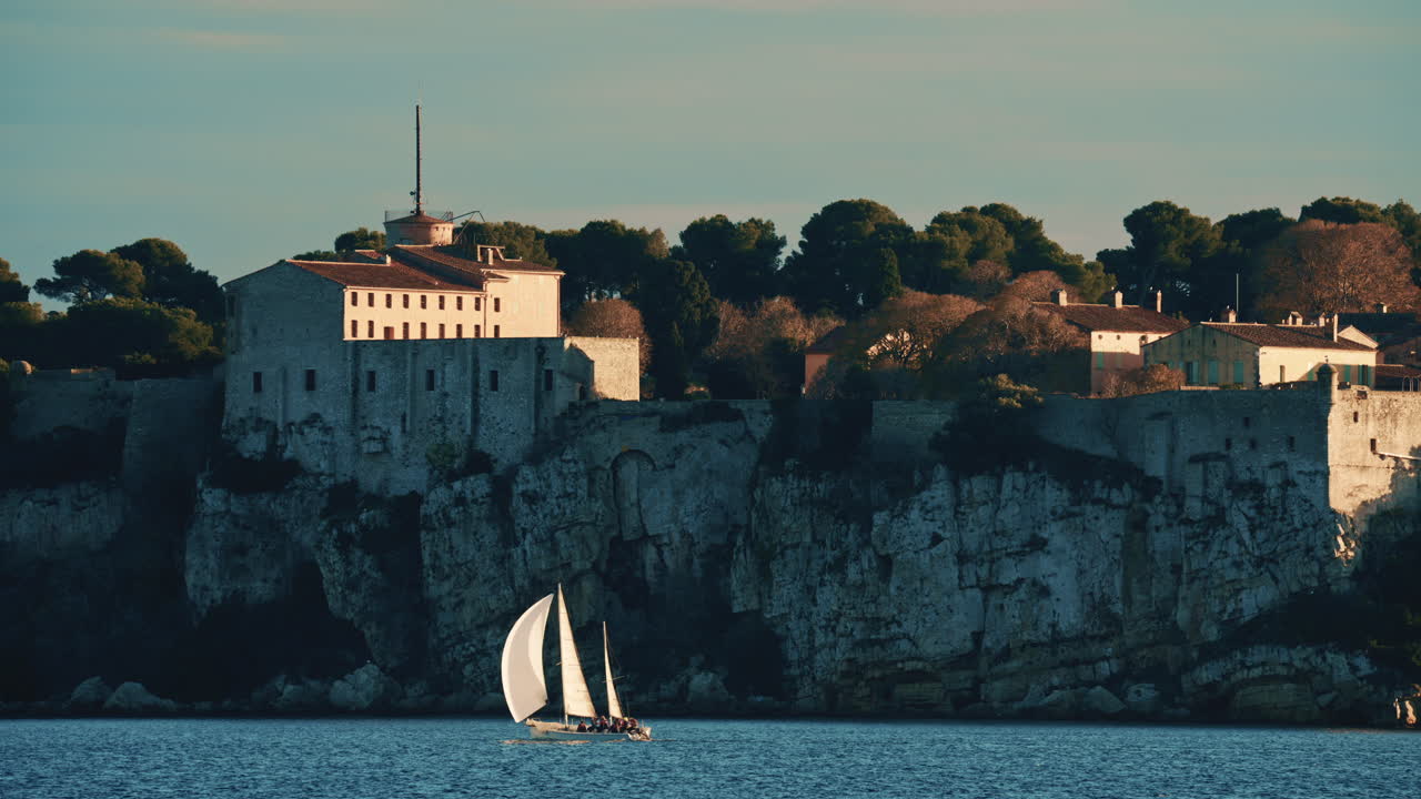 Barca a vela che galleggia sulle calme acque del Mediterraneo di fronte allo storico Fort Carré ad Antibes