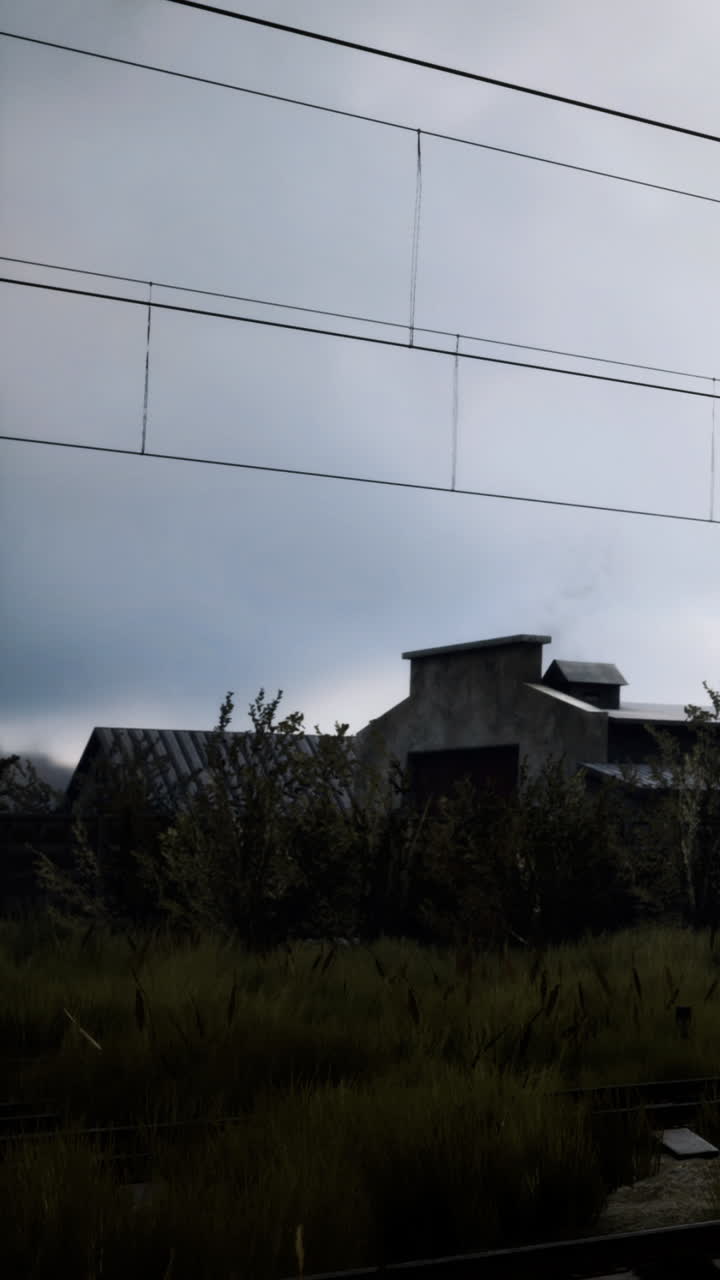 Edificio y vías de tren bajo un cielo nublado en un entorno rural.