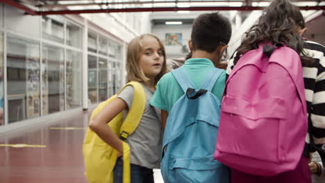 primer plano de niño con anteojos y mochila caminando hacia sus compañeros de clase a lo largo del corredor de la escuela