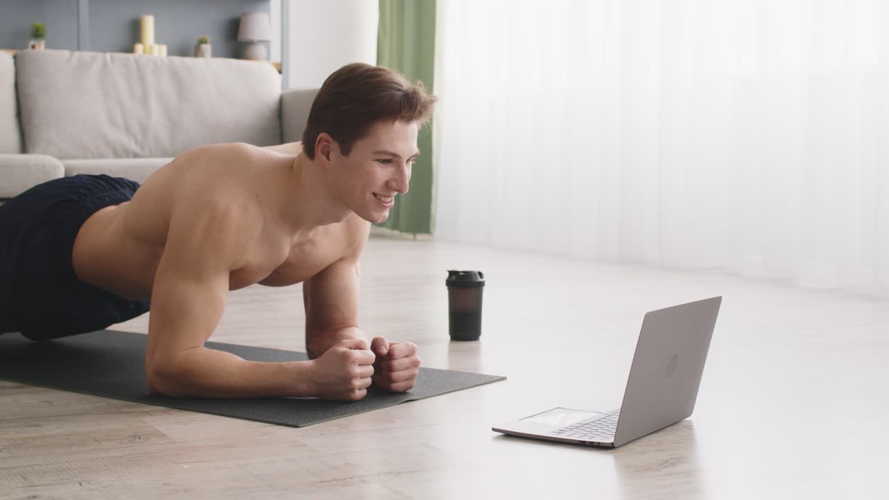 hombre haciendo ejercicio de tabla en casa mientras ve un video de entrenamiento en línea